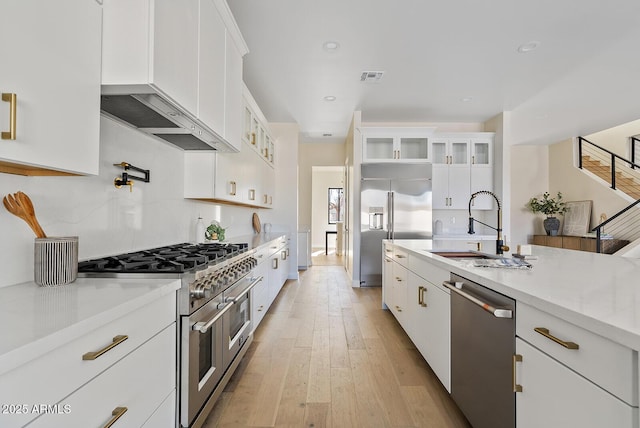 kitchen with sink, white cabinetry, premium appliances, light stone countertops, and light wood-type flooring