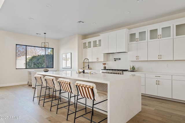 kitchen featuring sink, light hardwood / wood-style flooring, a center island with sink, a kitchen breakfast bar, and white cabinets