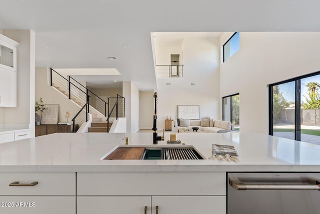 kitchen featuring white cabinetry, stainless steel dishwasher, plenty of natural light, and light stone counters