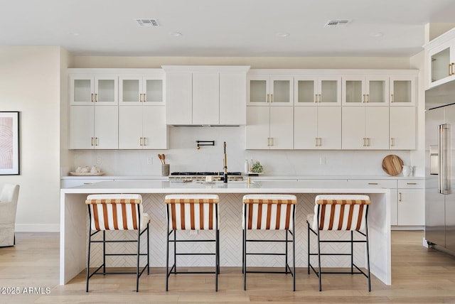 kitchen featuring a kitchen bar, a kitchen island with sink, built in fridge, and white cabinets