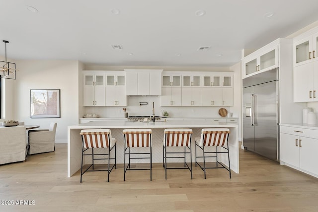 kitchen featuring built in fridge, an island with sink, a breakfast bar, and decorative light fixtures