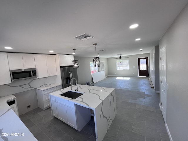 kitchen with a center island with sink, appliances with stainless steel finishes, hanging light fixtures, white cabinetry, and a sink