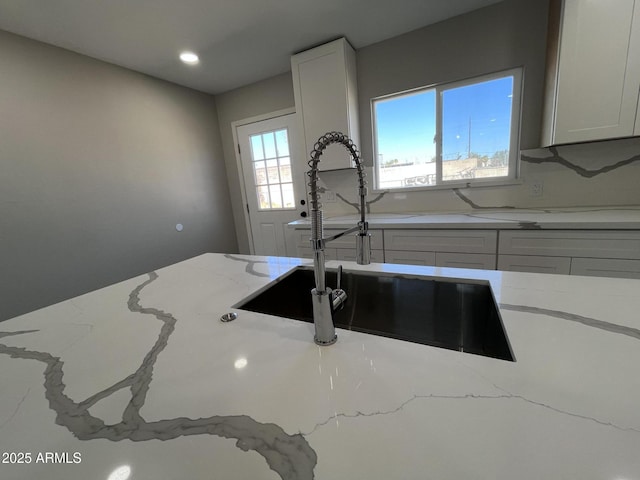 interior details featuring recessed lighting, white cabinets, a sink, and light stone countertops