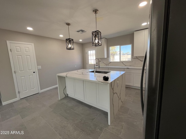 kitchen with a center island with sink, visible vents, white cabinets, freestanding refrigerator, and pendant lighting