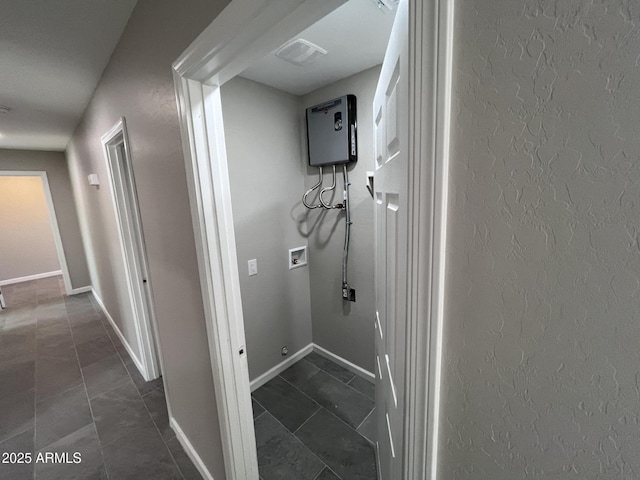 hallway featuring a textured wall, dark tile patterned floors, visible vents, and baseboards