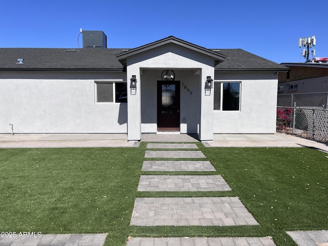 rear view of house with a yard, fence, and stucco siding