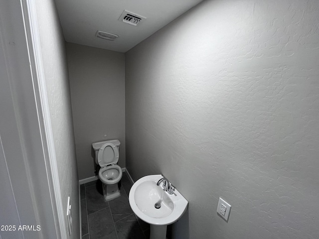 bathroom with visible vents, a textured wall, toilet, a sink, and tile patterned flooring