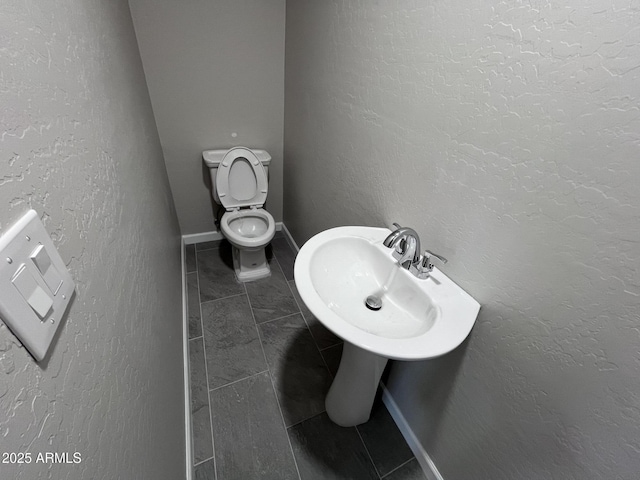 half bathroom with a textured wall, tile patterned flooring, toilet, and baseboards