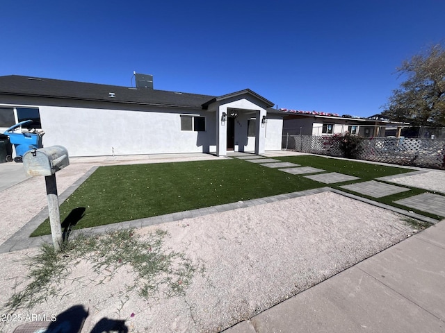 view of front of home with a front yard, fence, and stucco siding