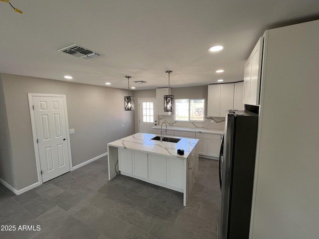 kitchen featuring pendant lighting, visible vents, freestanding refrigerator, white cabinets, and an island with sink