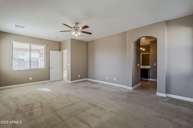 unfurnished room with baseboards, visible vents, arched walkways, a ceiling fan, and light colored carpet