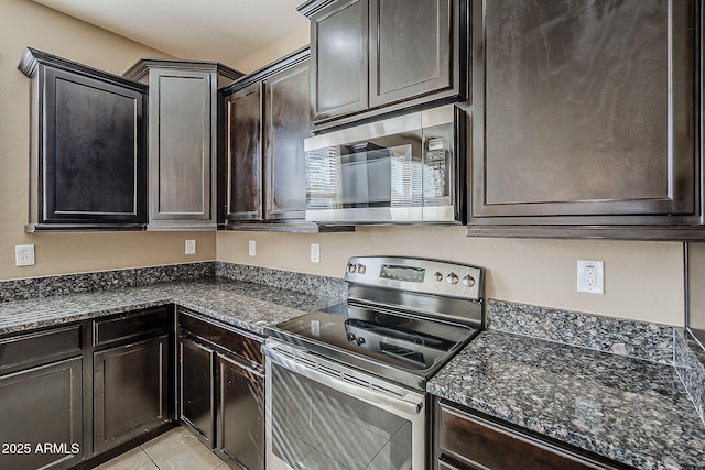 kitchen featuring light tile patterned floors, dark brown cabinets, appliances with stainless steel finishes, and dark stone counters