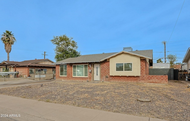 ranch-style home with roof with shingles, brick siding, and fence