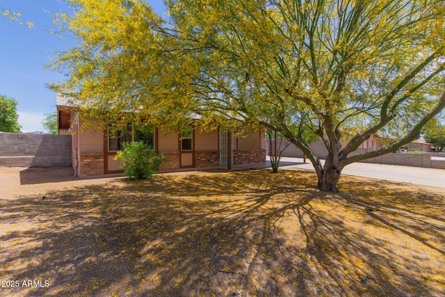 view of property hidden behind natural elements featuring brick siding and fence