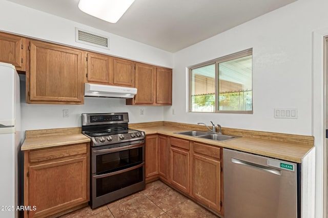 kitchen with appliances with stainless steel finishes, a sink, light countertops, under cabinet range hood, and visible vents