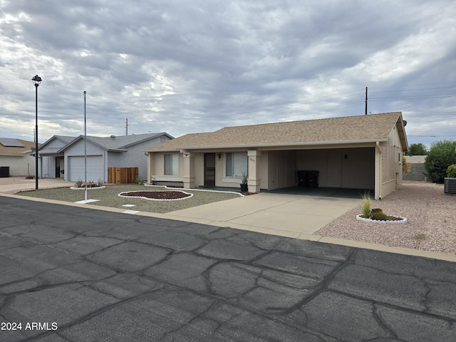 ranch-style home featuring an attached carport, central AC unit, a shingled roof, fence, and driveway