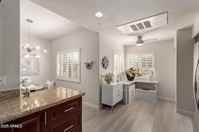 kitchen featuring dark brown cabinets, light wood finished floors, light stone counters, and baseboards