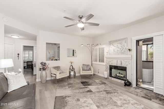 living room with a ceiling fan, a fireplace, baseboards, and wood finished floors