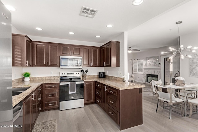 kitchen featuring dark brown cabinetry, visible vents, a premium fireplace, light stone countertops, and stainless steel appliances