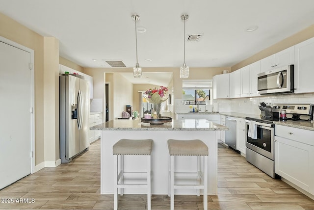 kitchen with stainless steel appliances, a center island, white cabinets, and light stone counters