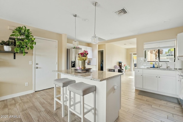 kitchen with sink, light stone countertops, white cabinets, a kitchen island, and stainless steel fridge with ice dispenser