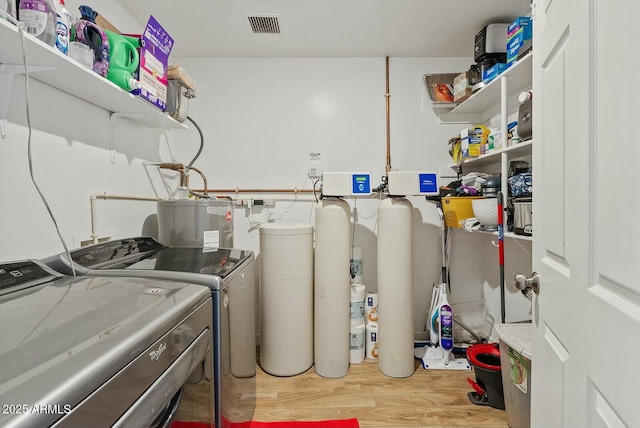 clothes washing area featuring hardwood / wood-style flooring, washing machine and dryer, and water heater