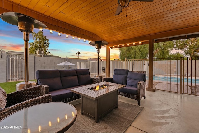 patio terrace at dusk with ceiling fan, a fenced in pool, and an outdoor living space with a fire pit