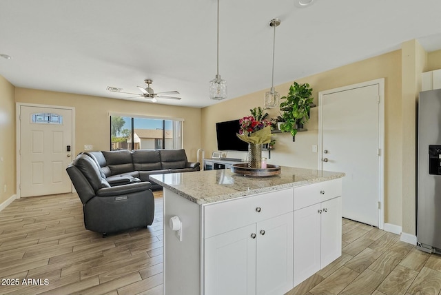 kitchen featuring white cabinetry, light stone counters, a kitchen island, stainless steel fridge with ice dispenser, and decorative light fixtures