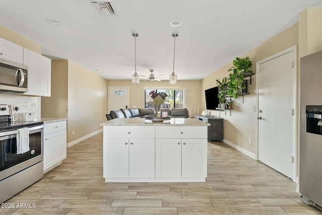 kitchen with hanging light fixtures, backsplash, stainless steel appliances, white cabinets, and a kitchen island