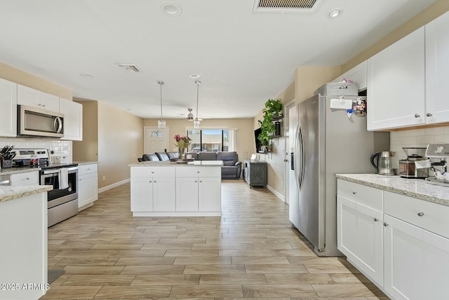 kitchen with pendant lighting, appliances with stainless steel finishes, white cabinetry, light stone counters, and tasteful backsplash