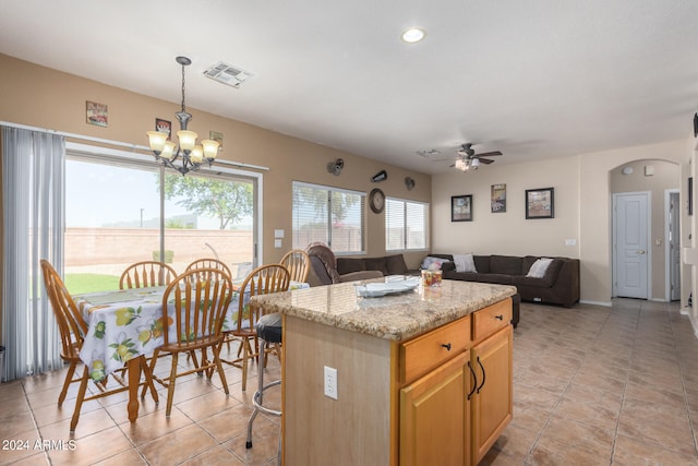 kitchen featuring ceiling fan with notable chandelier, a kitchen island, a breakfast bar, decorative light fixtures, and light stone counters