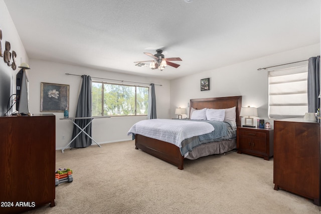 bedroom with ceiling fan, light colored carpet, and a textured ceiling