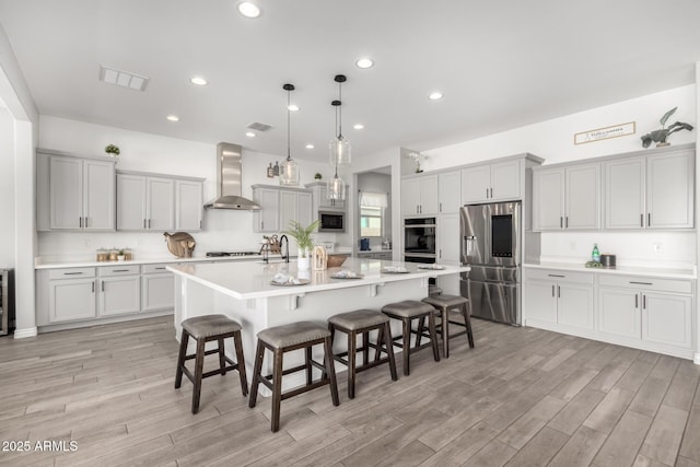 kitchen featuring pendant lighting, a large island with sink, wall chimney range hood, stainless steel fridge with ice dispenser, and a breakfast bar area