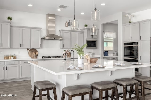 kitchen with wall chimney range hood, a kitchen island with sink, a breakfast bar area, and pendant lighting