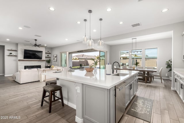 kitchen featuring pendant lighting, dishwasher, a fireplace, an island with sink, and sink