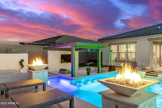 pool at dusk with an outdoor fire pit and a patio