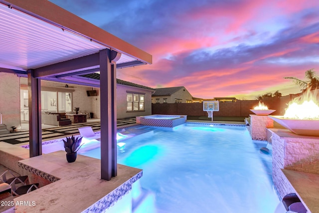 pool at dusk with pool water feature, an in ground hot tub, a patio, and exterior bar