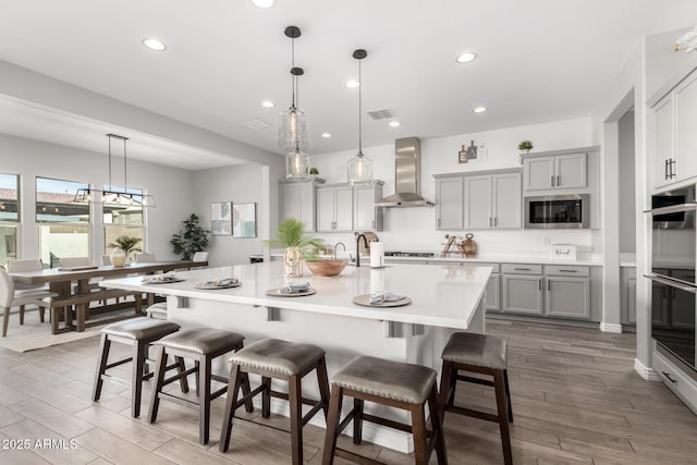 kitchen featuring decorative light fixtures, a breakfast bar, wall chimney exhaust hood, and built in microwave