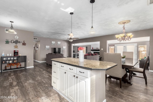 kitchen with white cabinetry, dark wood-type flooring, dark stone countertops, pendant lighting, and ceiling fan with notable chandelier