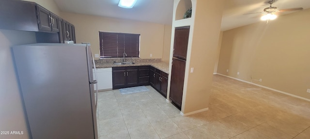 kitchen with dishwasher, light tile patterned floors, light stone counters, a sink, and freestanding refrigerator