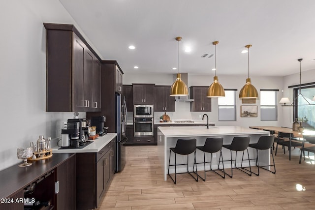 kitchen featuring a center island with sink, hanging light fixtures, dark brown cabinetry, a breakfast bar area, and stainless steel appliances