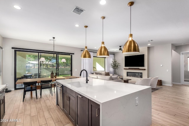 kitchen featuring dark brown cabinets, sink, light hardwood / wood-style floors, hanging light fixtures, and an island with sink