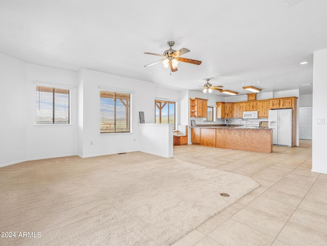 unfurnished living room featuring light carpet, a healthy amount of sunlight, baseboards, and a ceiling fan