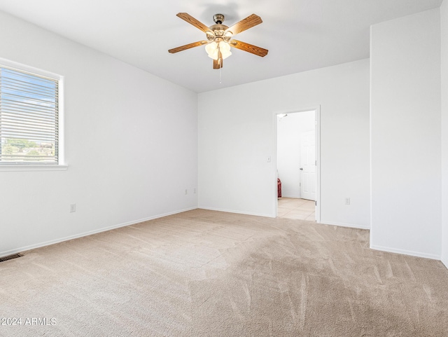 unfurnished room with a ceiling fan, light colored carpet, visible vents, and baseboards