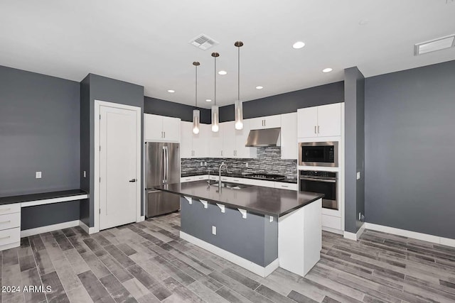 kitchen featuring stainless steel appliances, dark wood-type flooring, decorative light fixtures, white cabinetry, and an island with sink