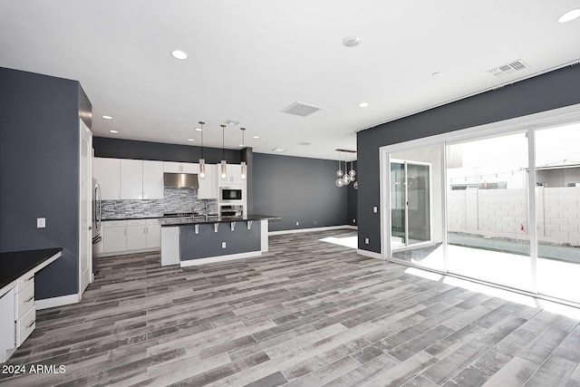 kitchen with white cabinetry, decorative backsplash, wood-type flooring, decorative light fixtures, and a kitchen island with sink