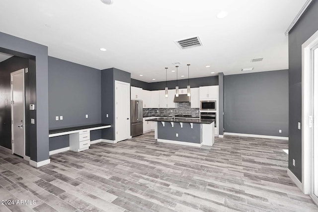 kitchen with white cabinets, light hardwood / wood-style flooring, built in desk, appliances with stainless steel finishes, and decorative light fixtures