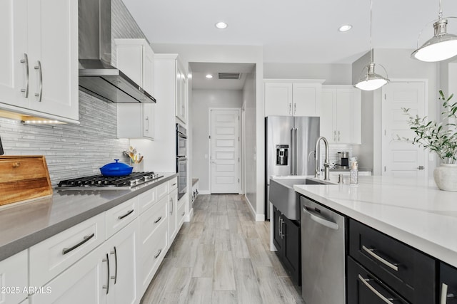 kitchen with pendant lighting, white cabinetry, appliances with stainless steel finishes, and wall chimney range hood