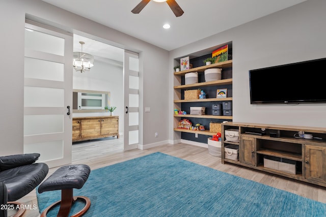 sitting room with ceiling fan with notable chandelier, light hardwood / wood-style flooring, and built in shelves