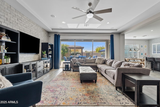 living room featuring ceiling fan, brick wall, and light wood-type flooring